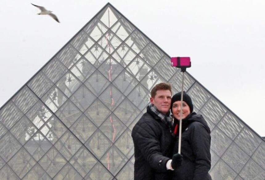 Casal tira foto com o pau de selfie em frente ao museu do Louvre, em Paris (Foto: Remy de la Mauviniere/AP)